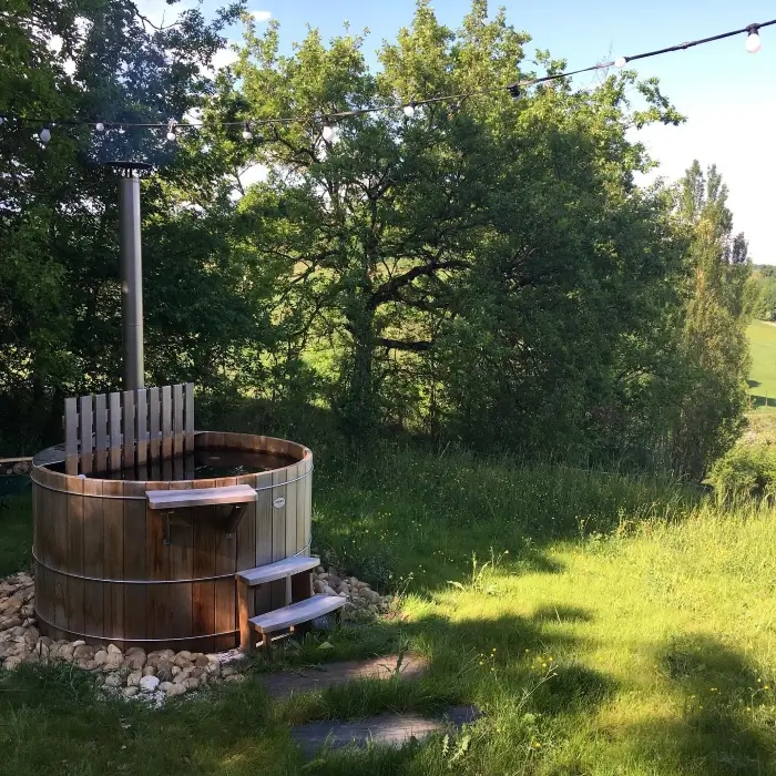 Un bain nordique : un grand bassin en bois rempli d'eau chaude chauffée par un poêle à bois, installé à l'extérieur. 