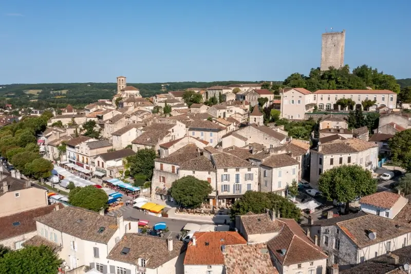 Montcuq-village-tour-marche Vue aérienne du village médiéval de Montcuq un dimanche, jour de marché, dominé par sa tour-donjon du 12e siÚcle.