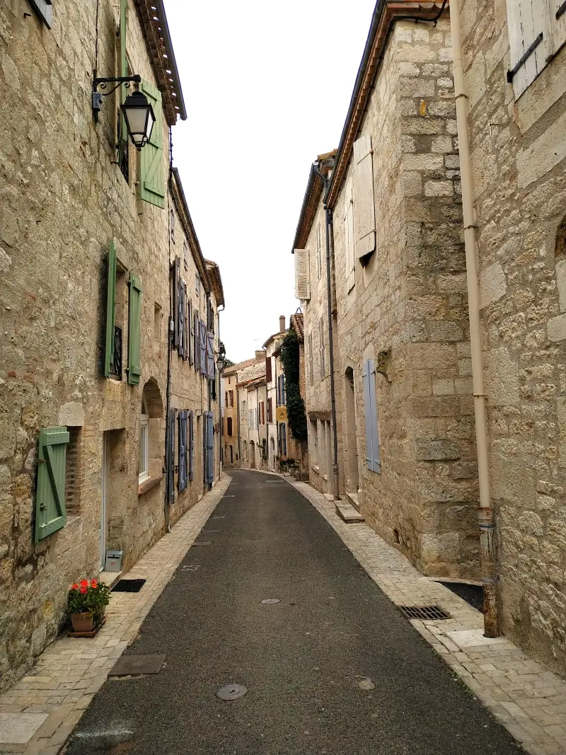 La rue Montmartre à Montcuq : maisons en pierre blanche, volets bleus et verts.