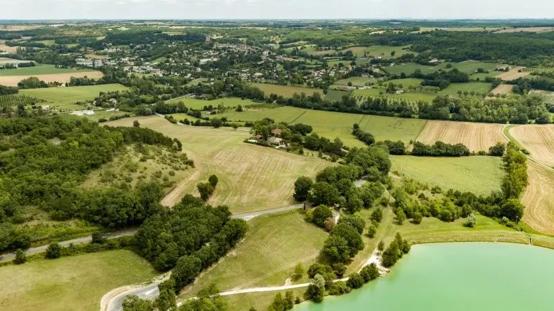 Vue aérienne sur le village de Montcuq au milieu des collines du Quercy Blanc, et du lac de baignade tout proche.